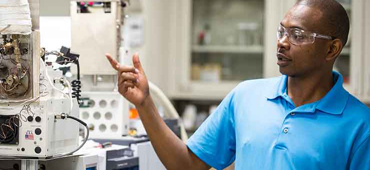 Photo of a man wearing protective glasses in a lab pointing at some equipment