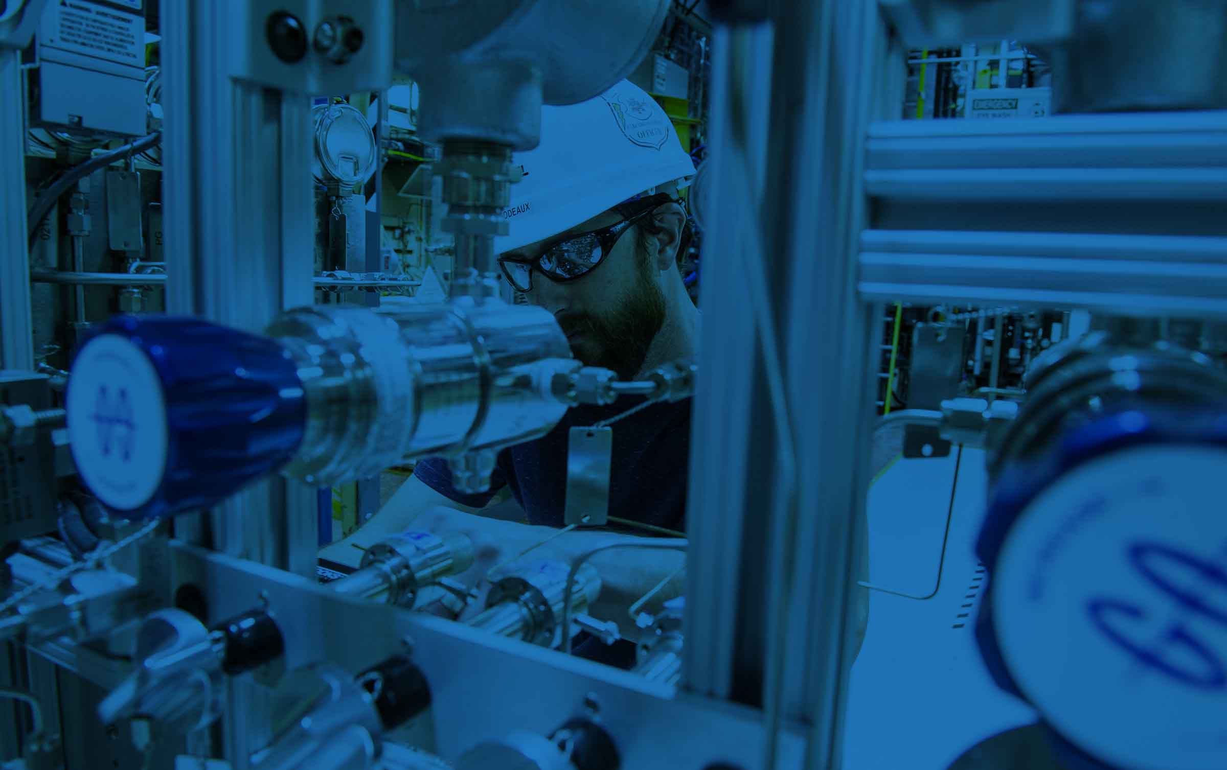 Man with a helmet around some mechanical equipment